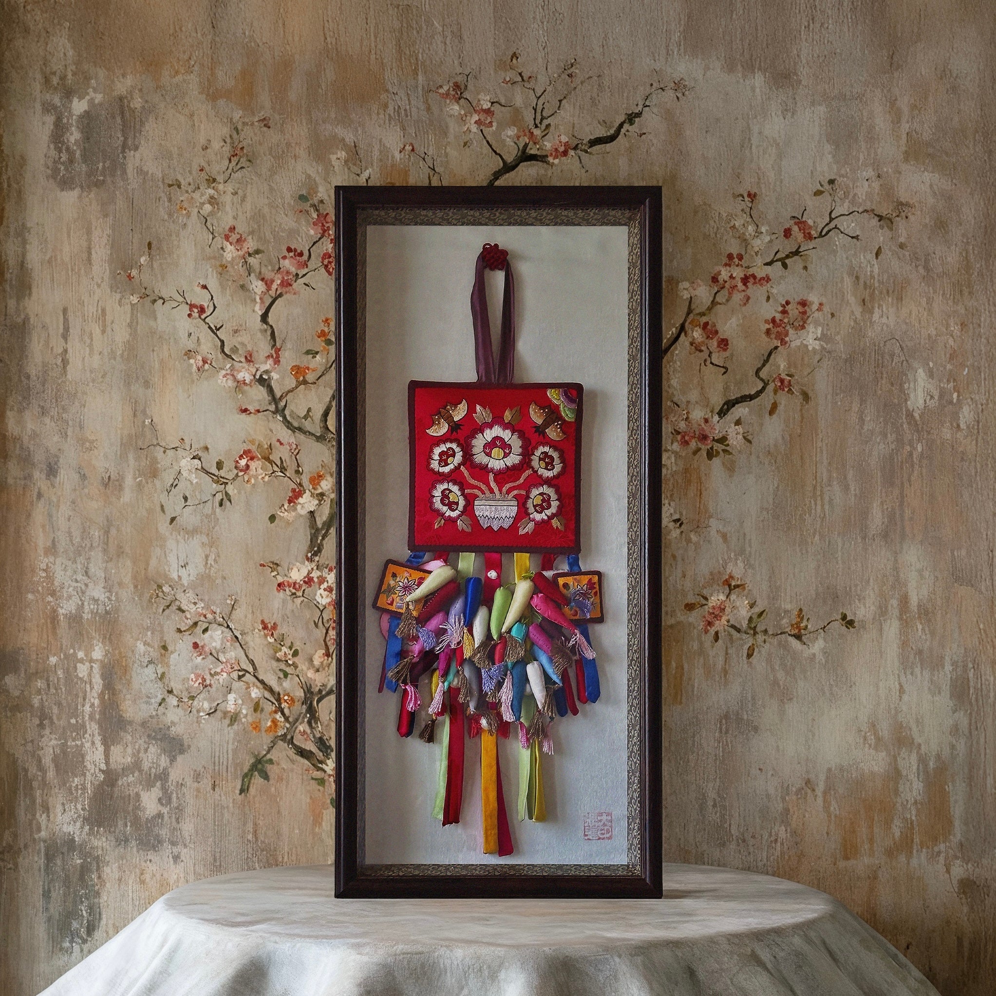 A large framed Korean embroidered key tassel norigae, showcasing silk-stitched peonies and a bat motif on deep fabric, evoking grace, fortune, and tradition.
