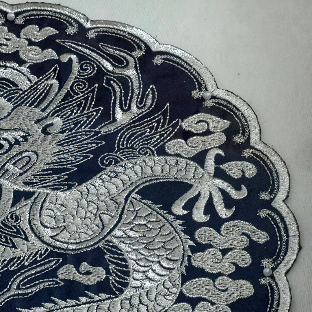 Close-up of silver embroidered dragon design on a dark fabric background