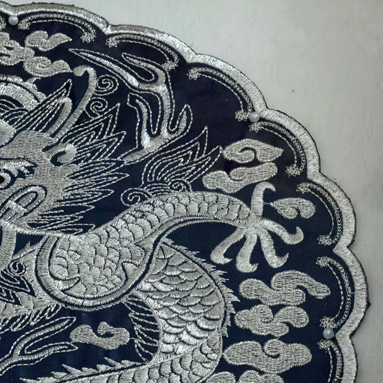 Close-up of silver embroidered dragon design on a dark fabric background