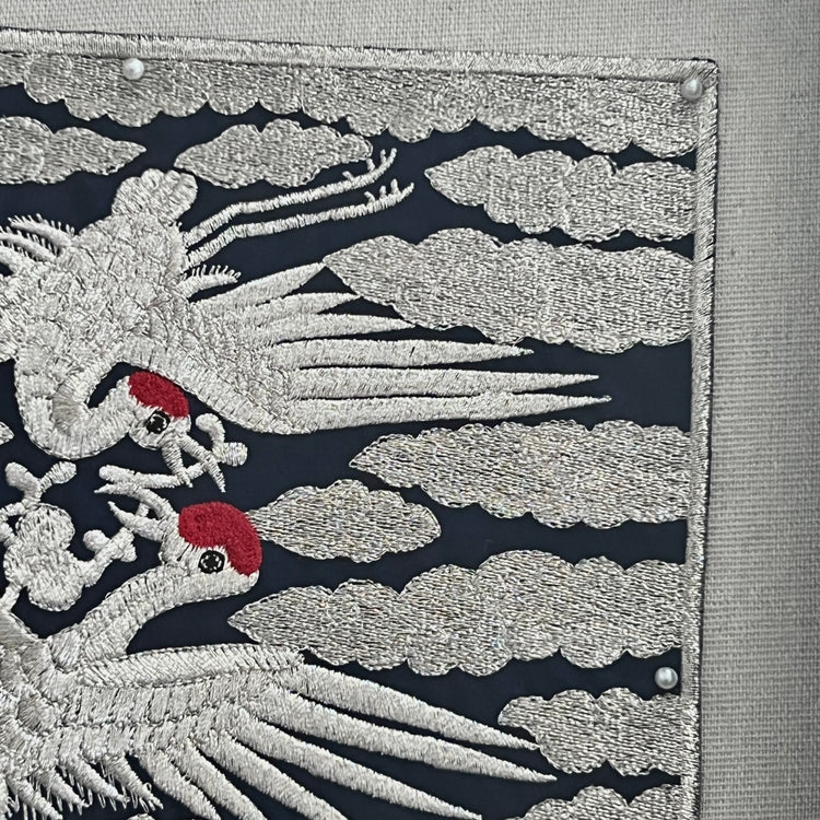 Embroidered design of cranes on a dark background with clouds.
