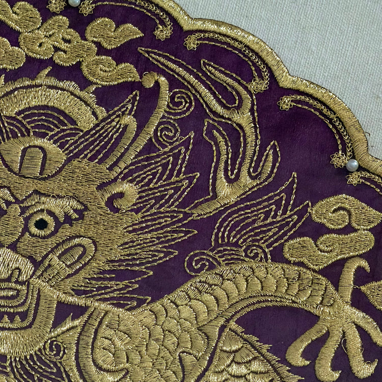 Gold embroidered dragon design on purple fabric