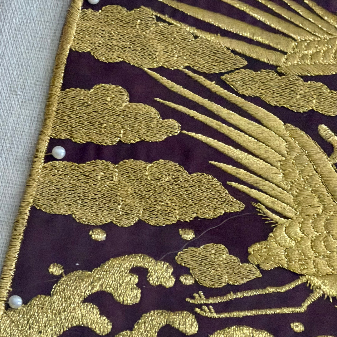 Close-up of gold embroidered fabric with cloud and leaf patterns on a dark background