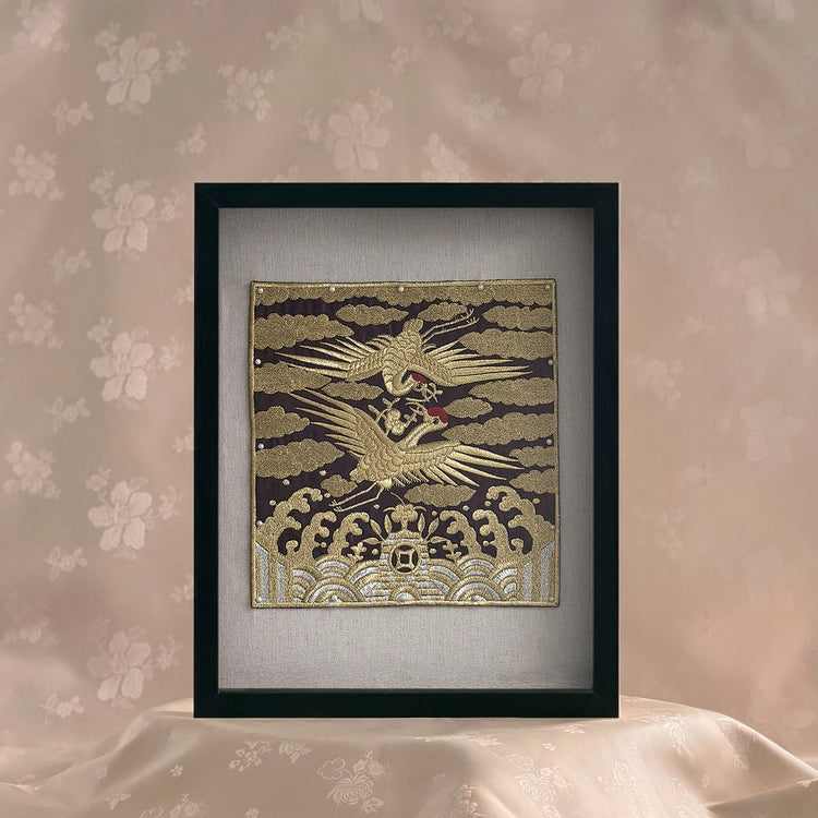 Framed artwork with a gold and black design of a bird on a textured wall.