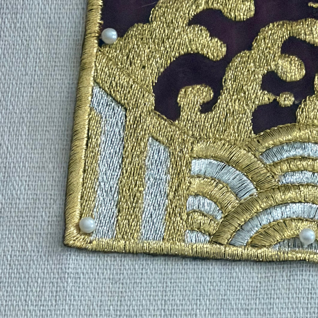 Close-up of an embroidered patch with gold, silver, and black design on a gray background