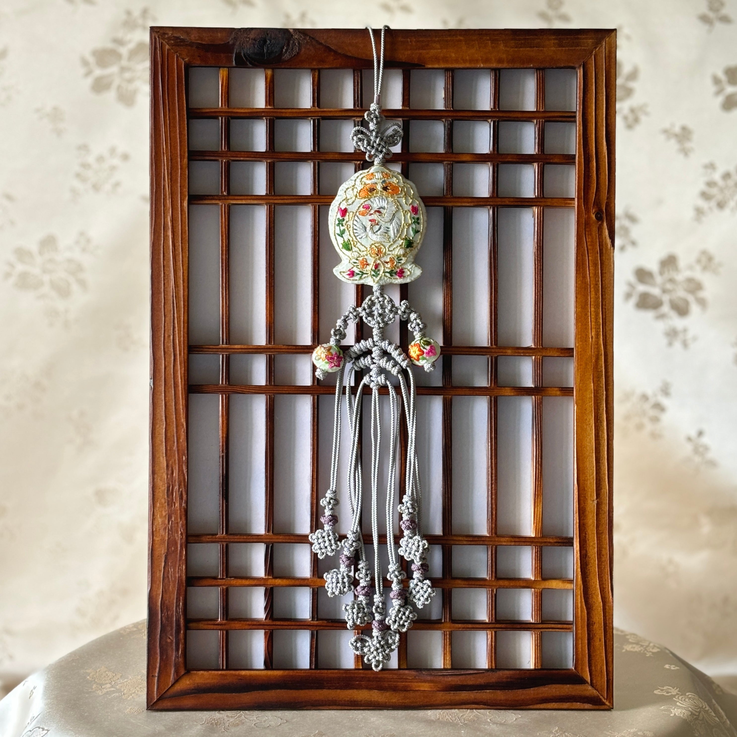 A traditional Korean Norigae hanging in a wooden frame, featuring a double crane pattern with multicolored details.