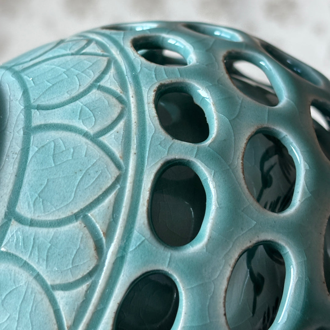 Close-up of a teal ceramic object with intricate patterns and holes