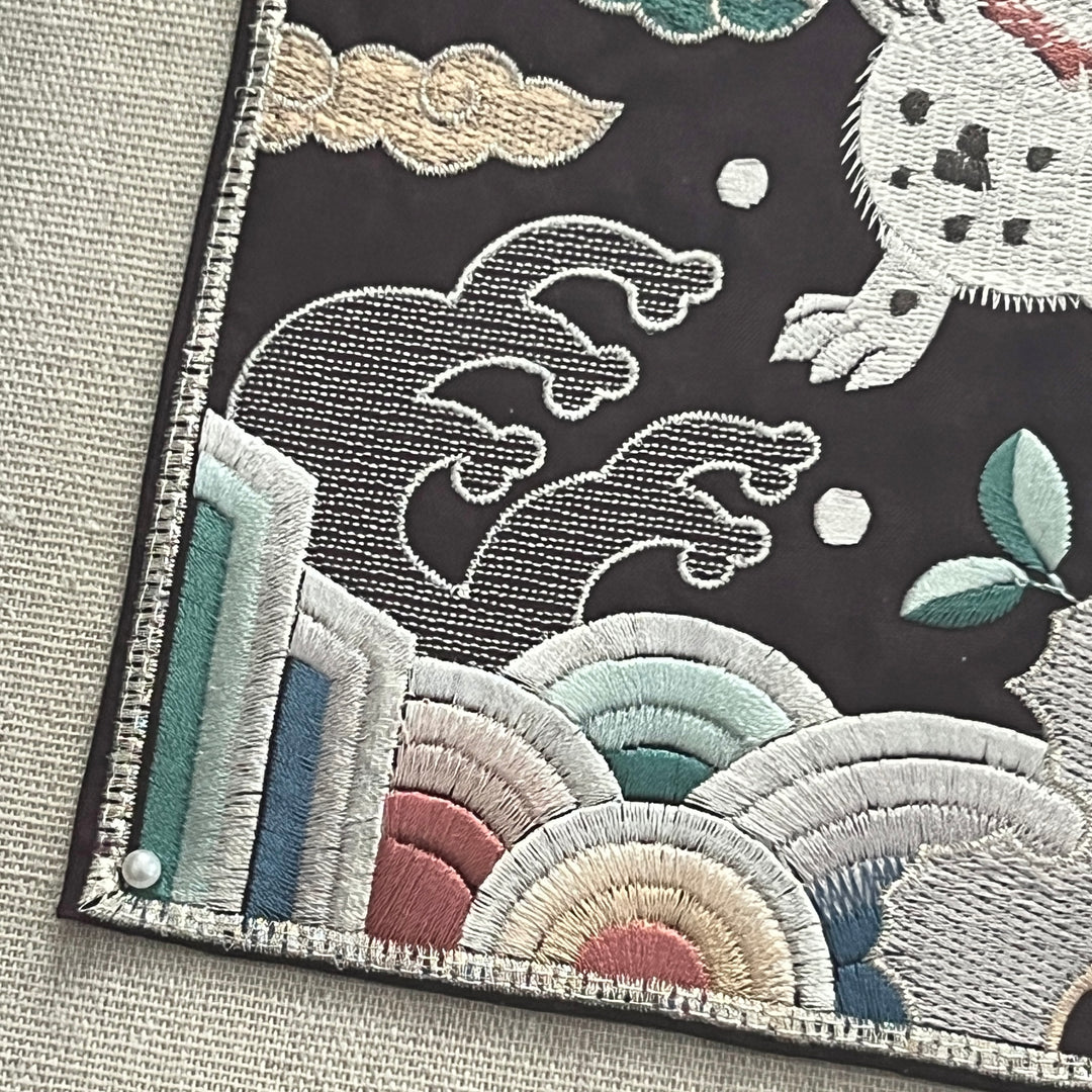 Embroidered design with tigers and clouds on a textured fabric background