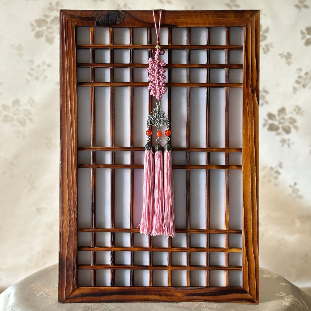 A pink tassel hanging from a wooden frame, possibly part of a traditional norigae decoration.