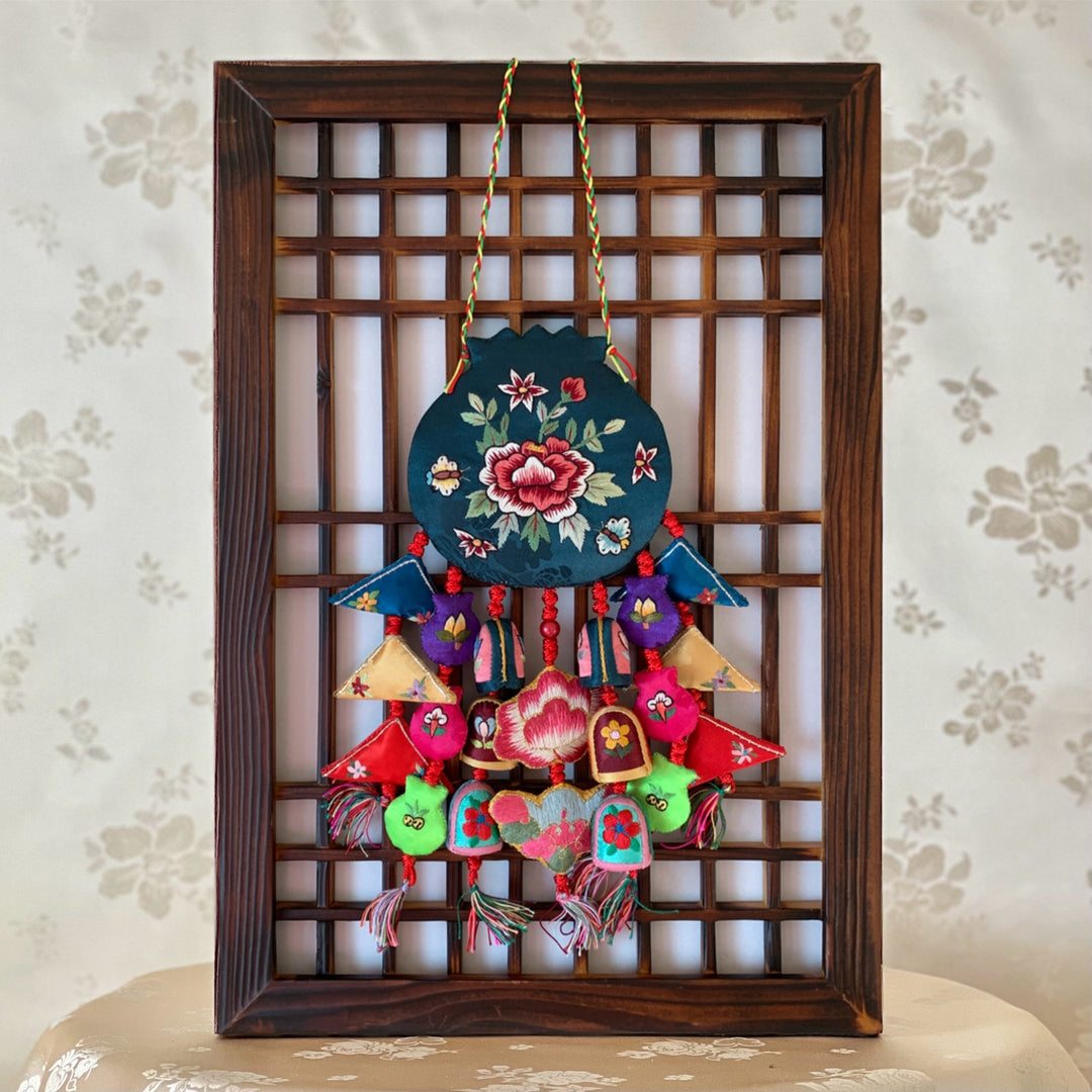 A traditional Korean norigae with embroidered peony pattern, hanging on a wooden frame.