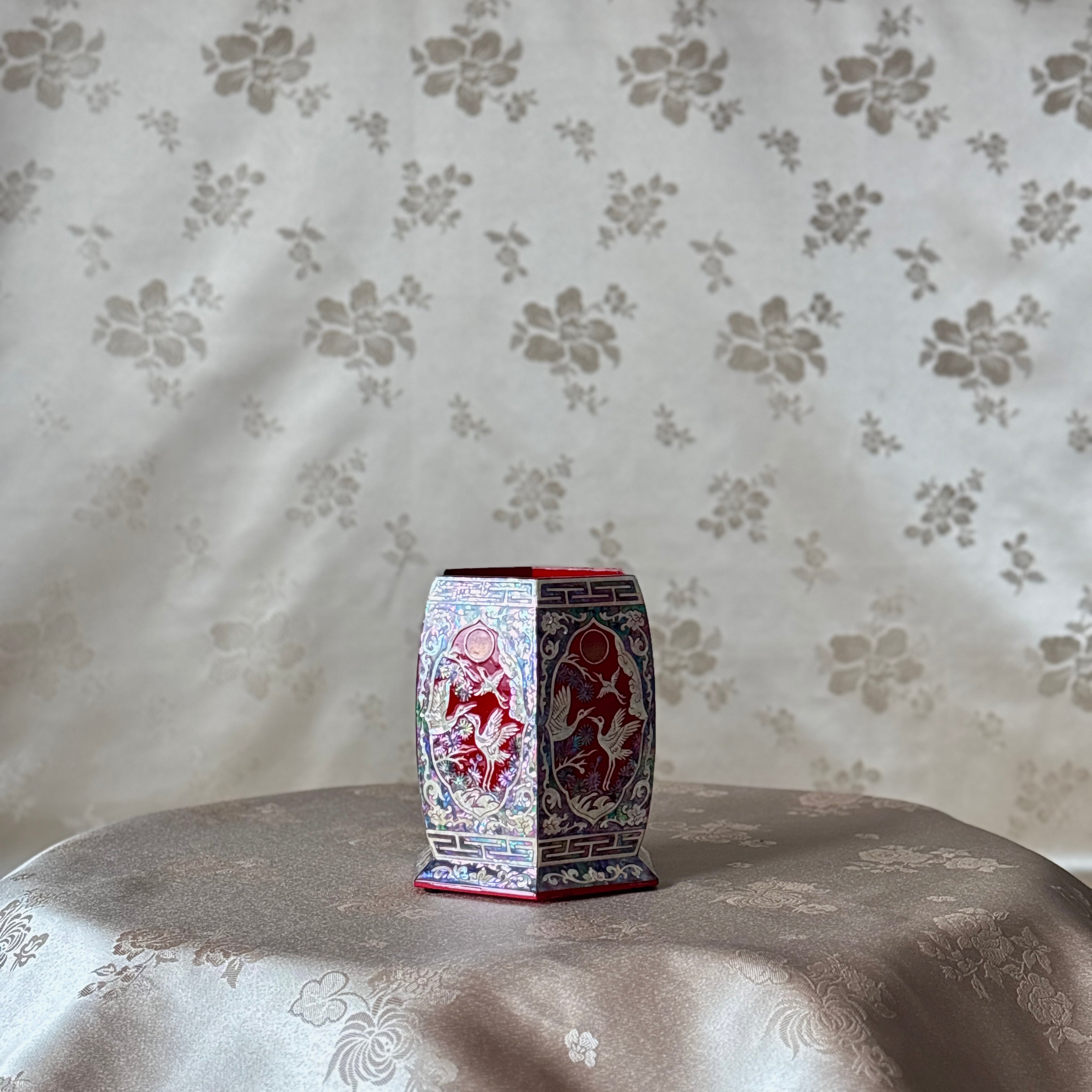 Decorative hexagonal pencil holder with red and white patterns on a floral-patterned surface.