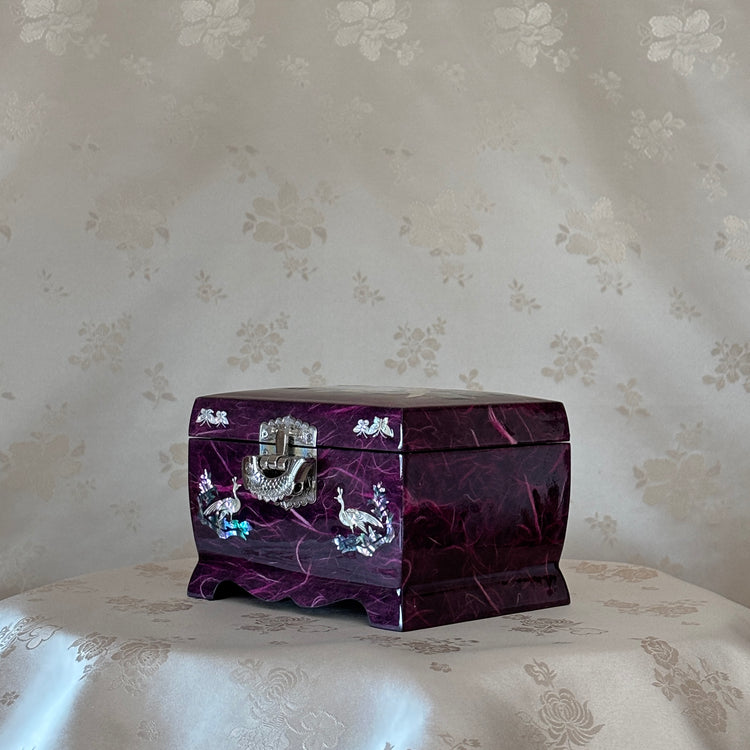 Purple jewelry box with silver accents on a floral-patterned surface