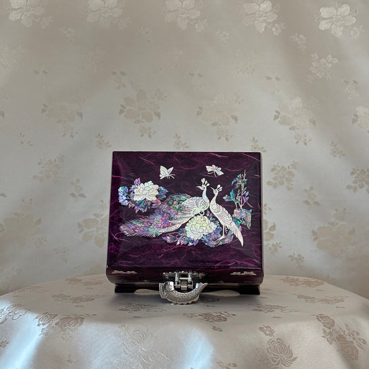 Decorative jewelry box with peacock design on a floral-patterned surface