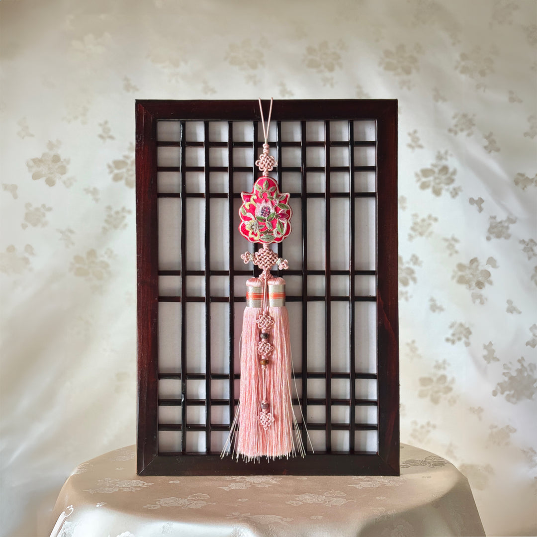 A Korean norigae featuring a blooming peony embroidery with a double tassel, displayed within a wooden frame.