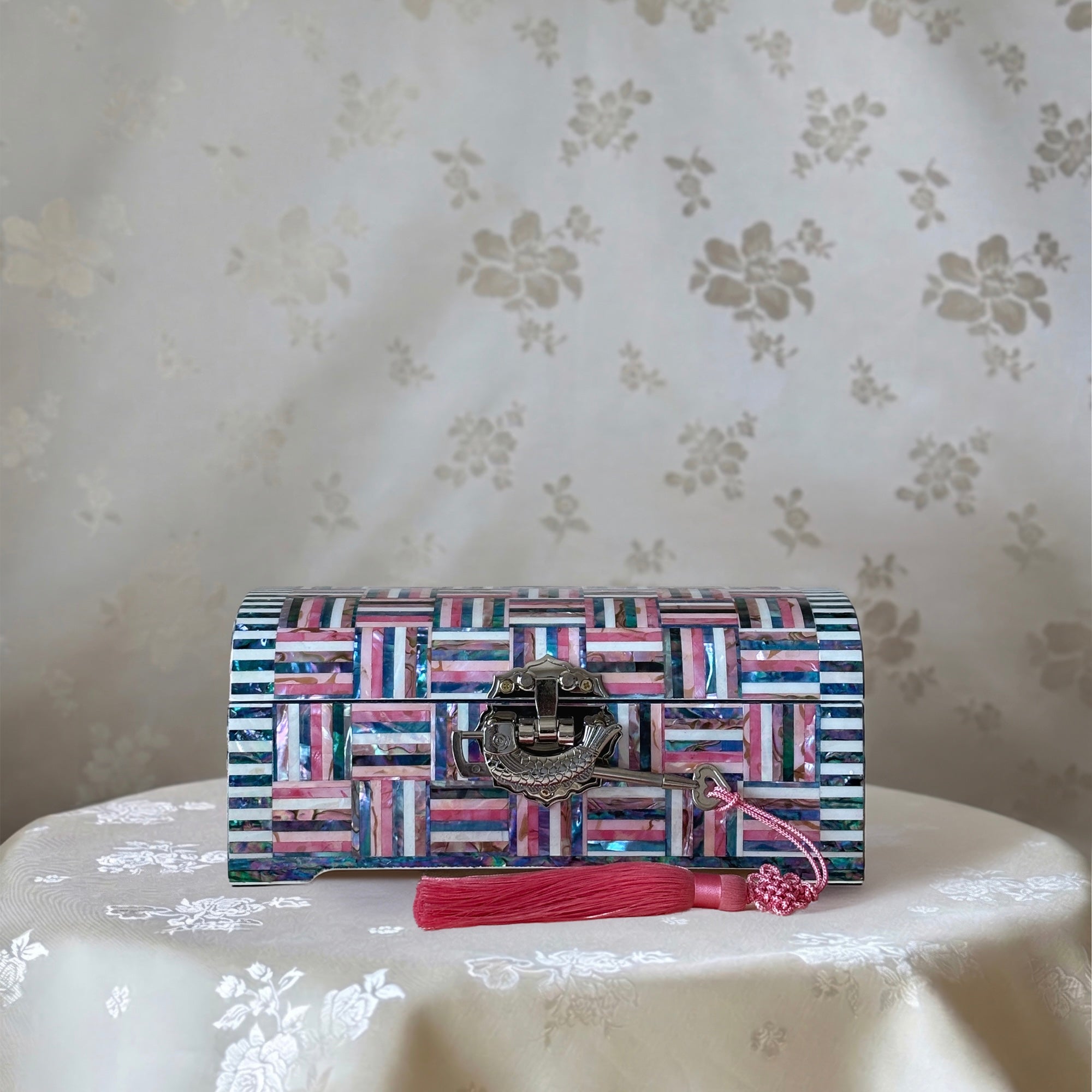Multicolored patterned clutch bag with a pink tassel on a floral-patterned surface