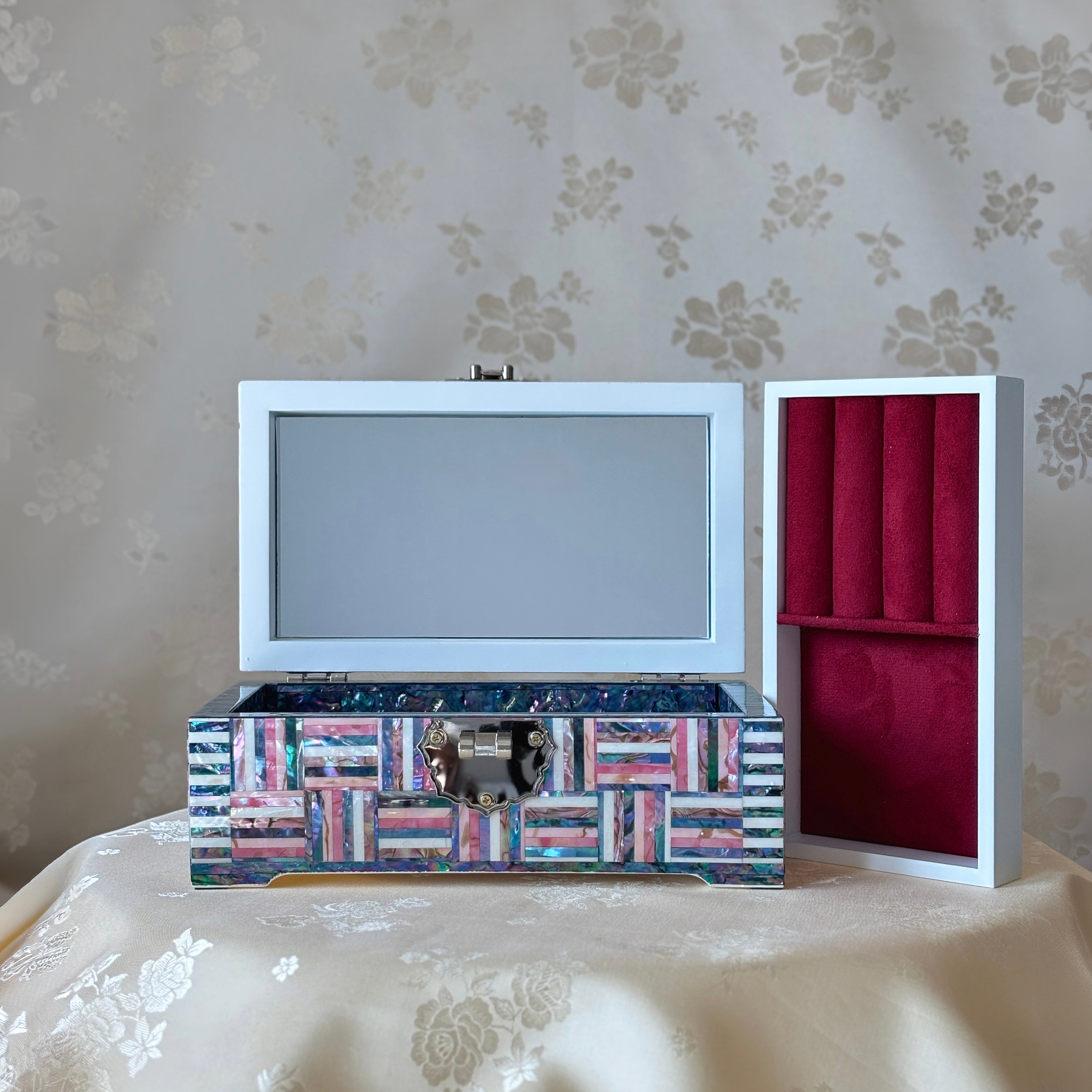 Decorative jewelry box with a mirror and red interior on a floral-patterned surface