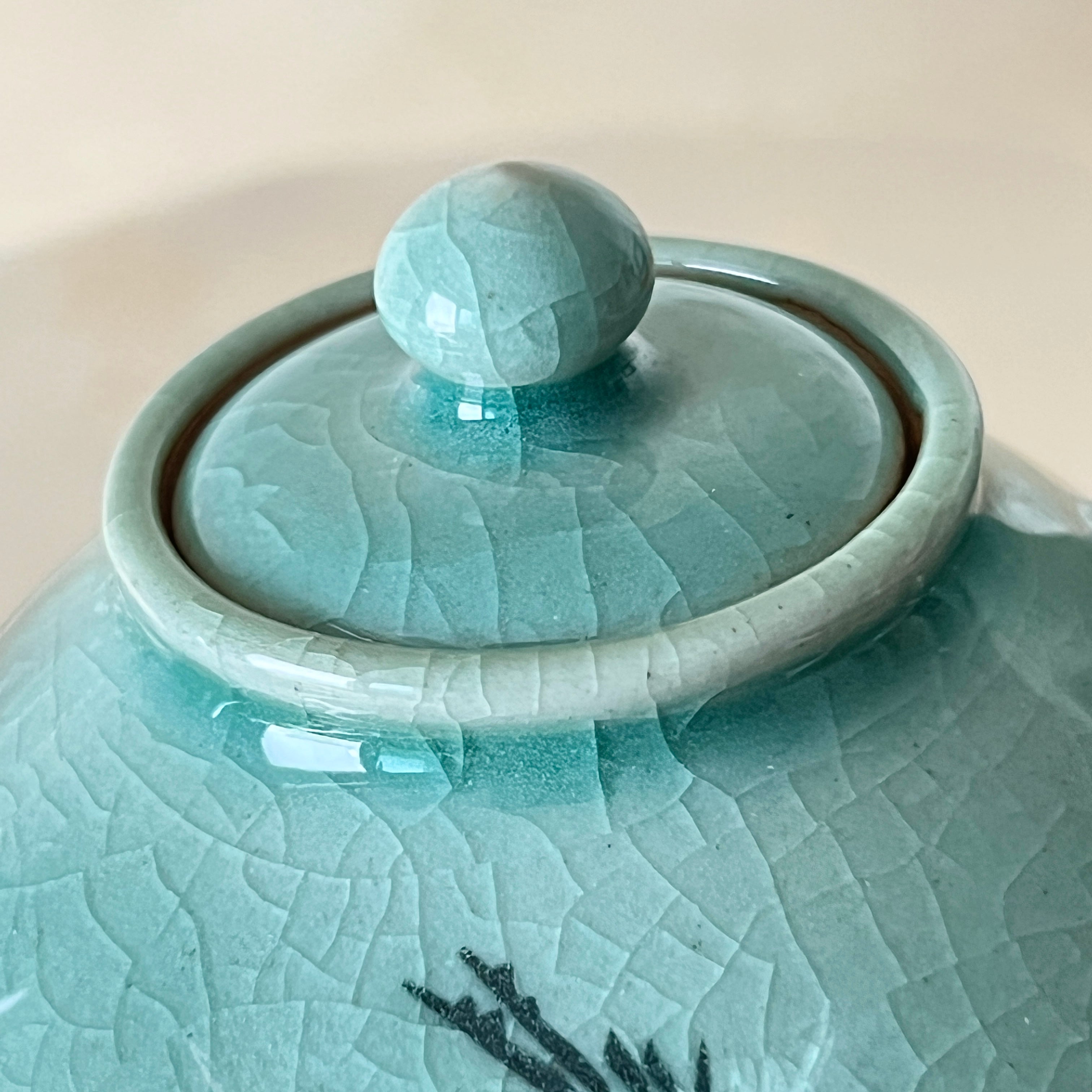 Light blue ceramic jar with textured surface and spherical handle on a beige background korean