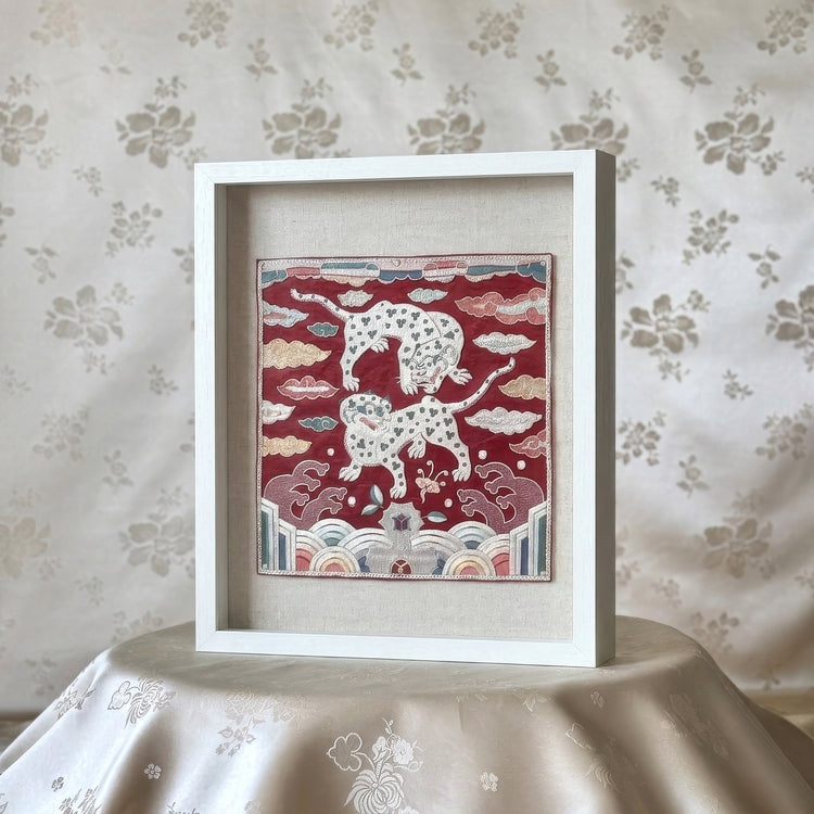 Framed artwork with a red background and white tiger animals on a floral-patterned tablecloth.
