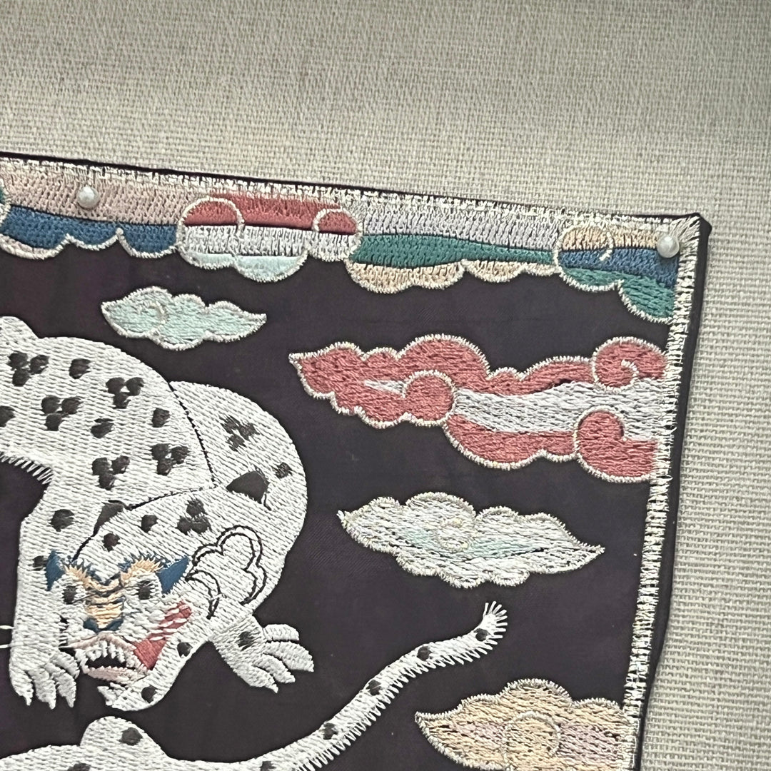 Embroidered fabric with a tiger design and cloud patterns on a dark background.