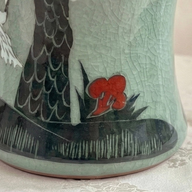 Ceramic vase with detailed design of a bird and red flower on a textured surface.